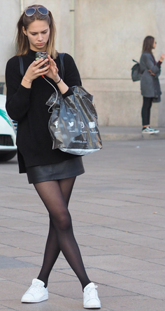 Woman in a black sweater and leather skirt looking at her phone on a street