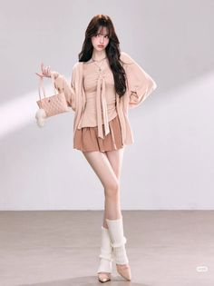 Woman with long hair wearing a cardigan, shorts, and leg warmers, holding a small bag