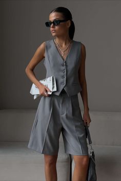 Woman in a gray vest and shorts holding a newspaper and bag