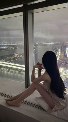 Woman with long dark hair sitting by a window overlooking a city at night