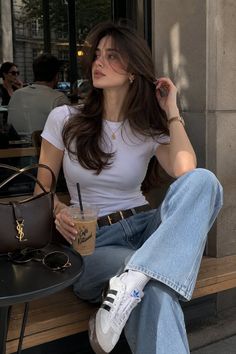Woman with long brown hair in a white t-shirt and jeans at an outdoor cafe