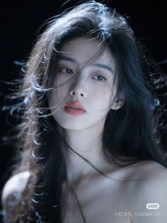 Woman with long black hair and exposed shoulders against a dark background