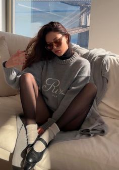 Woman in a gray sweater and black tights sitting on a couch indoors