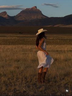Woman in a cowboy hat and boots in a field with mountains at golden hour