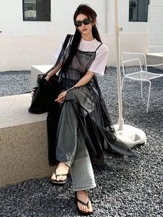 Woman in sunglasses, a white t-shirt, and a black sheer dress sitting outdoors