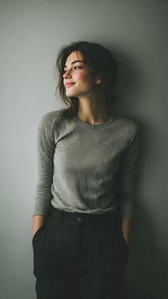 Woman with long hair in a grey shirt and black pants looking to the side