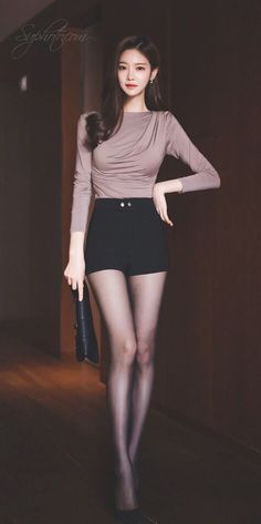 Woman with long hair wearing black shorts and tights, holding a clutch bag
