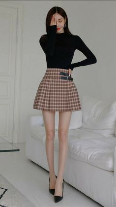 Woman in a black long-sleeve top and plaid skirt posing indoors