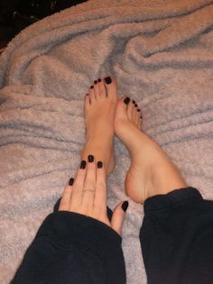 A person's feet and hand with black nail polish on a gray blanket