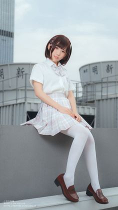 Woman in a school uniform with a plaid skirt and white tights sitting outdoors