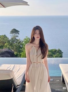 Woman in a light halter cutout dress by an infinity pool with an ocean view