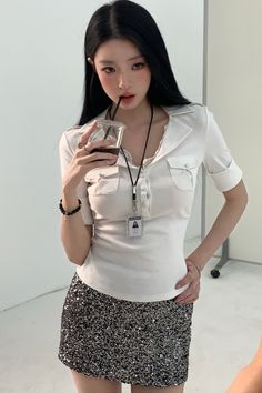 Woman with long black hair in a white polo shirt and sequin skirt drinking from a cup