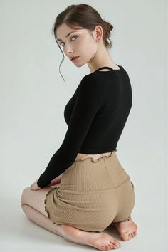 Woman in a black long-sleeve top and brown shorts kneeling in a studio
