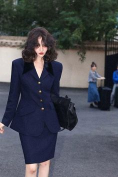Woman in a navy blue suit with short wavy hair and red lipstick outdoors
