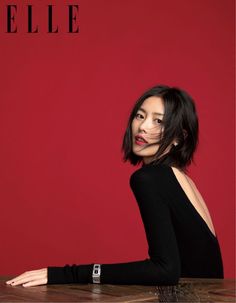 Woman with short black hair in a black top with an exposed back against a red background