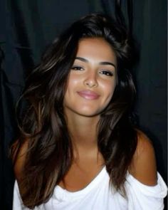 Woman with long dark hair and dimples wearing a white off-shoulder shirt