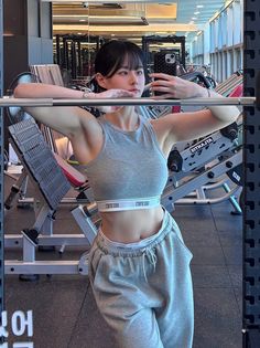 Woman in a grey crop top and sweatpants posing in a gym mirror selfie