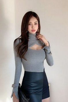 Woman with long hair wearing a gray cutout top and black skirt indoors