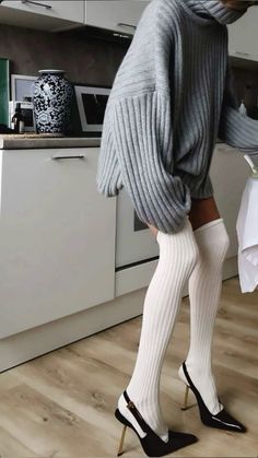 Woman in an oversized sweater, white thigh-high socks, and high heels in a kitchen