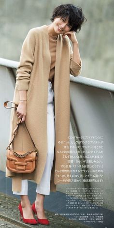 Woman in a long beige cardigan, white pants, and red heels, holding a brown handbag