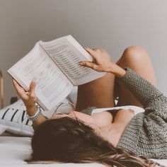 Woman with long hair reading a book while lying on a bed