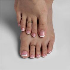 Feet with a french pedicure and toe rings on a light background