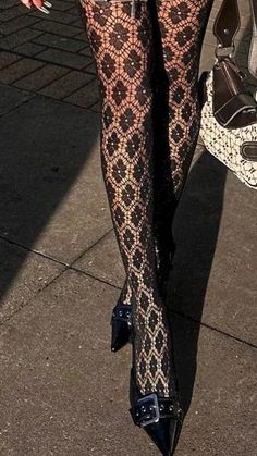 Person wearing black lace tights and buckled heels on a sunny outdoor surface
