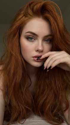 Woman with long red hair and blue eyes, with a hand near her mouth