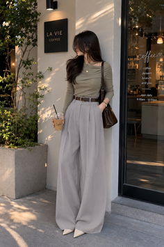 Woman in a long sleeve top and wide leg pants outside a coffee shop
