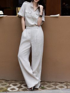 Woman in a light-colored linen shirt and wide-leg pants leaning against a wall