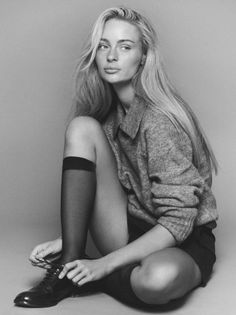 Woman with long blonde hair wearing a grey sweater and black shorts, tying her shoe