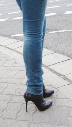 Person wearing blue jeans and black high heel boots on a sidewalk