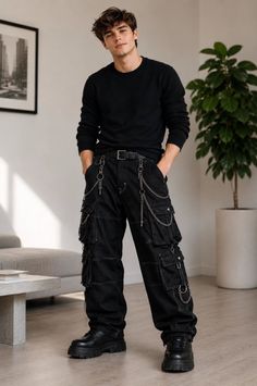 Man in black cargo pants with chains and a black sweater standing indoors