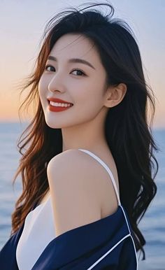 Woman with long dark hair and red lipstick smiling outdoors at sunset