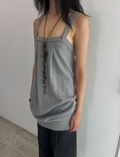 Person in a gray top and black pants with a long necklace indoors