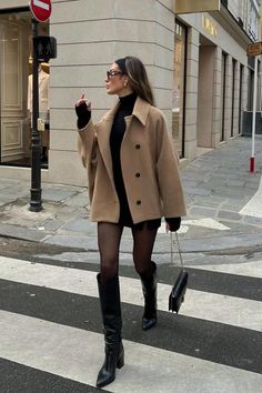Woman in a camel coat and black outfit crossing a street