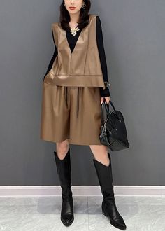 Woman in a brown leather vest and shorts with black long boots and handbag