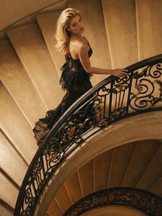 Woman in a black lace dress on a spiral staircase looking over her shoulder
