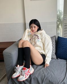 Woman with short black hair wearing a hoodie, shorts, and sneakers sitting on a couch