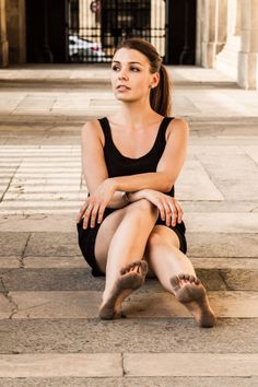 Woman in a black dress with dirty feet sitting on a stone floor outdoors