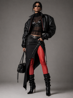 Woman in a cropped leather jacket, sheer top, and red tights posing in a studio