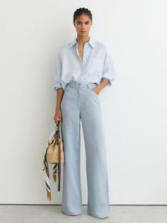 Woman in a light blue shirt and wide leg pants holding a bucket bag