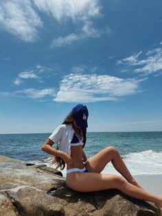 Woman in a bikini and baseball cap sitting on rocks at the beach