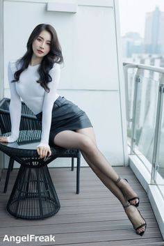 Woman in a white top and black leather skirt posing on a balcony