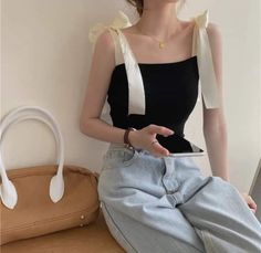 Woman in a black top with ribbon straps and light wash jeans holding a phone
