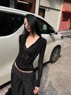 Woman with long black hair wearing a sheer top and black bra on a street