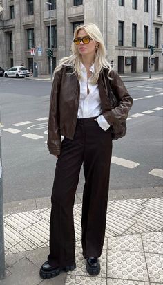 Woman with blonde hair wearing a brown leather jacket and wide leg pants on a city street