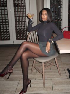 Woman in a dark turtleneck and mini skirt holding a cocktail indoors