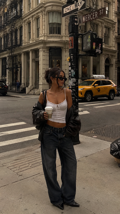 Woman in a white camisole, baggy jeans, and leather jacket on a city street