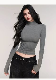 Woman with long black hair wearing a gray turtleneck and black jeans